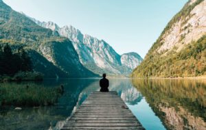 Zen moment sat on a pier over a calm lake with mountains in the background