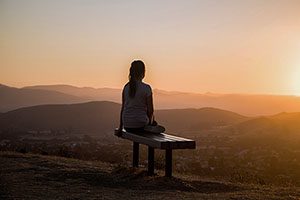 Zen moment of relaxation by woman on a bench on a hill at sunrise.