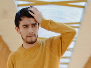 Picture of man on a bridge in yellow jumper with a migraine